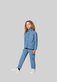 Lichtblauwe denimjack met twee borstzakken, knopenfront, gecombineerd met bijpassende cargobroek. Witte sneakers maken de outfit compleet.