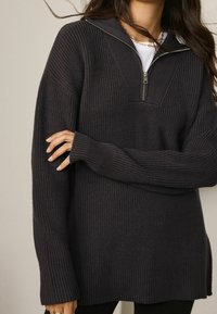 Maglione in maglia a costine grigio scuro con colletto a mezza zip e maniche lunghe con fori per il pollice. Vestibilità ampia con un motivo testurizzato.