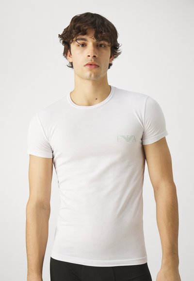 Camiseta de algodón blanca con mangas cortas y cuello redondo. Presenta un pequeño logo verde en la parte izquierda del pecho. Diseño suave y ajustado.