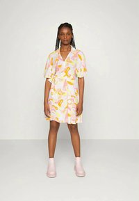 Vestido de envoltório de manga curta em rosa pastel com padrões abstratos em amarelo, laranja e branco, apresentando um cinto de laço e uma saia rodada.