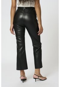 Svarta fusk-läder flare-byxor med hög midja, med en slät textur och en figursydd silhuett, bärs med svarta remmar-sandaler.