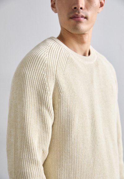 Beige knitted sweater with a textured pattern, featuring a round neckline and raglan sleeves. Material appears soft and warm.