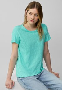 T-shirt à manches courtes et col rond en turquoise clair, fabriqué dans un tissu texturé avec un motif subtil, associé à un jean bleu clair.