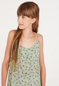 Groene bloemen-top met dunne bandjes, voorzien van een patroon van witte en zwarte bloemen, gemaakt van lichte stof en met een ronde halslijn.