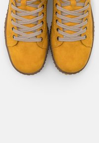 Zapatillas de ante amarillas con puntera redonda, cordones beige y suelas de goma, con detalles de costura en los lados.