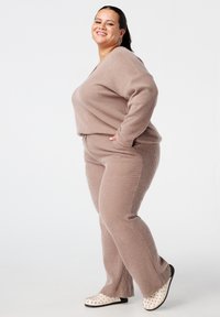 Tenue en tricot coordonnée de couleur marron clair, composée d'un pull décontracté à col en v et d'un pantalon assorti. Tissu texturé avec une coupe décontractée, associé à des sandales à clous.