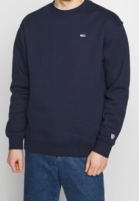 Sudadera azul marino hecha de una mezcla de algodón, con cuello y puños acanalados. Presenta un pequeño parche del logo en el pecho y en el puño. Corte clásico.