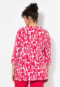 Rood-wit gestreepte top met driekwartmouwen, versierd met geometrische vormen. Zacht materiaal, ronde halslijn en een relaxte pasvorm.