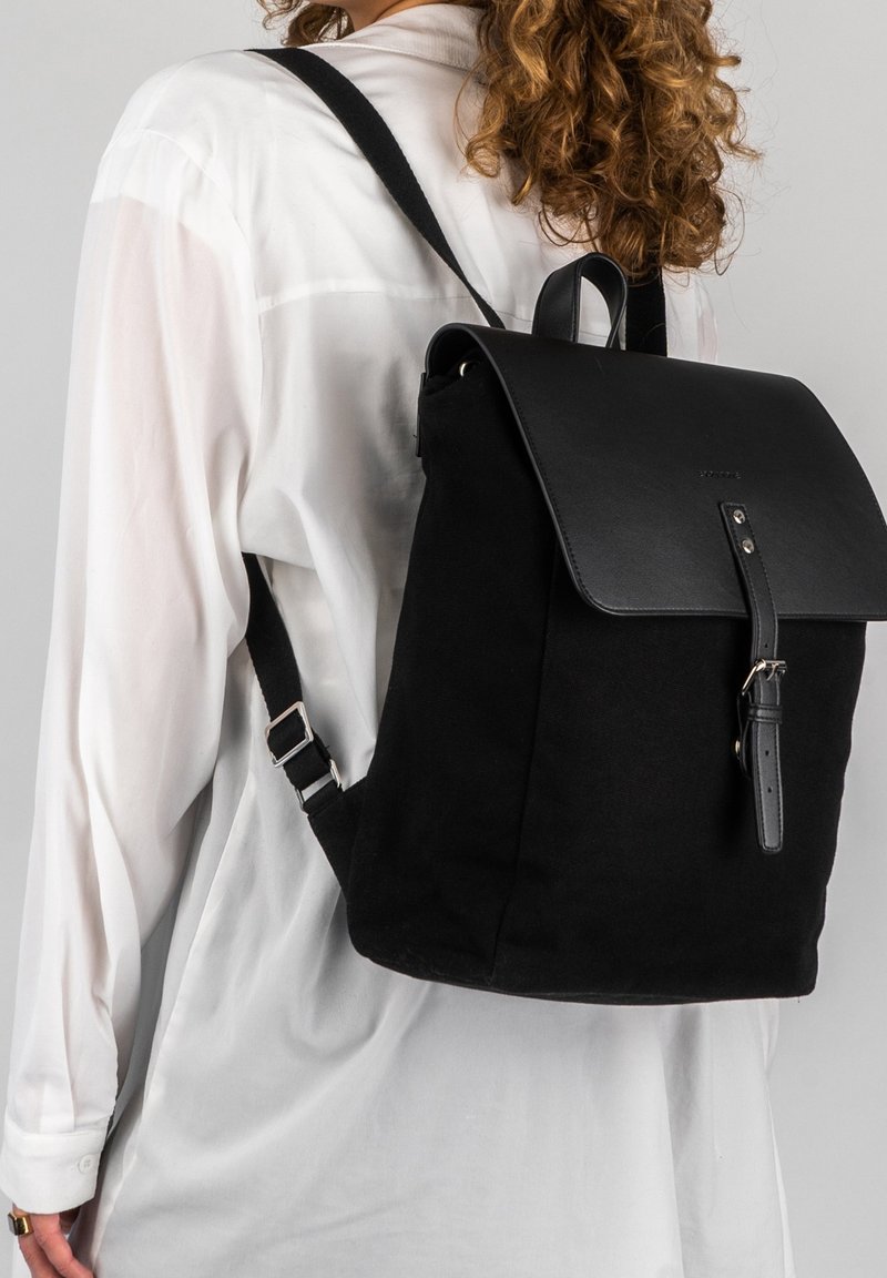 Zwarte canvas rugzak met een leren klep, verstelbare schouderbanden en metalen hardware. Eenvoudig ontwerp met een veilige sluiting en minimale details.