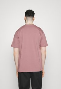 T-shirt à manches courtes en coton mauve, col rond, coupe décontractée, design uni, coutures visibles le long de l'ourlet et des manches, porté avec un pantalon noir.