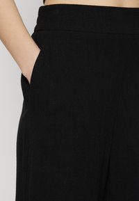 Sorte linbukser med sidelomme, glat tekstur, bredt design og tætsiddende talje. Enkel og minimalistisk konstruktion.