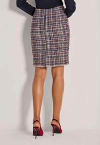 Tweed kokerrok in een multicolore ruitpatroon met franjes aan de onderkant. G draagt het met rode hoge hakken, wat een aansluitend ontwerp en een gladde textuur laat zien.
