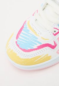 White sneaker with abstract patterns in pink, blue, and yellow, featuring a textured finish and white laces. Rubber sole with pink accents.