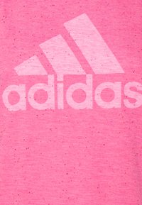 Tessuto rosa con macchie, grande logo Adidas bianco sbiadito e tre righe diagonali sopra il testo.