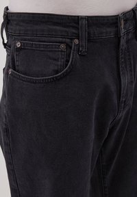Jean en denim noir coupe droite, avec poches avant et arrière, fermeture à bouton en métal et détails de couture subtils. Tissu texturé.