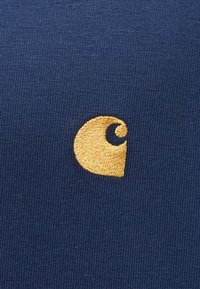 Temno modra tkanina z fino teksturo, ki na levi strani vsebuje zlate vezenine v spirali.