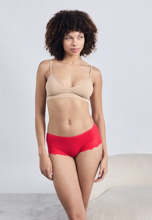 Nøgen bh med et snoet frontdesign, parret med røde boyshorts med blondeafslutning. Blødt stof, glat tekstur og buede former.