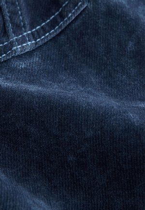 Mornarsko modra kordurova tkanina z mehko teksturo; vidni robovi in detajli šivov. Gladek površinski sloj z rahlim leskom.