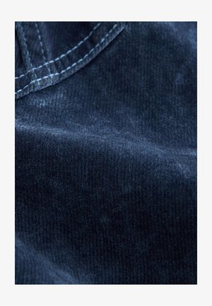 Marineblaue Kord-Stoff mit weicher Textur; sichtbare Rippen und Nahtdetails. Glatte Oberfläche mit leichtem Glanz.