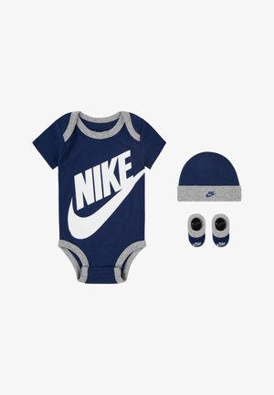Tamsiai mėlynas medvilninis bodysuit su pilkais akcentais ir dideliu baltu Nike logotipu, kartu su derančiu kepurėle ir batukais.