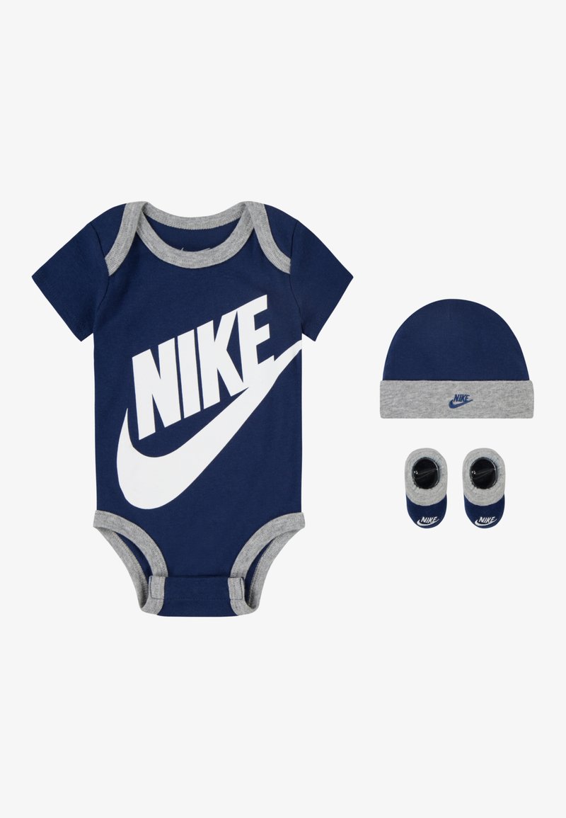 Tamsiai mėlynas medvilninis bodysuit su pilkais akcentais ir dideliu baltu Nike logotipu, kartu su derančiu kepurėle ir batukais.