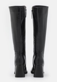 Botas de couro pretas até ao joelho com um salto robusto e fecho de zíper. A textura suave e os detalhes de costura vertical realçam o design.