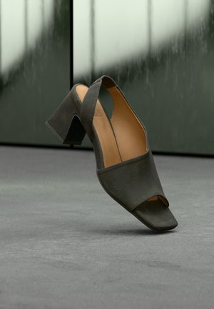 Svart, åpen tå hælsandal med et elegant design, som har en lett teksturert overflate og en kantete blokkhæl. Myk, tanfarget innerfór.