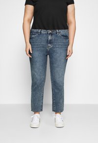 Jeans de mezclilla en azul claro, corte recto, con un acabado desgastado, cinco bolsillos y cierre de botón. Combinados con zapatillas blancas.