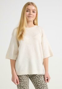 Jasnobeżowy, oversize sweter z krótkimi rękawami, z dzianiny o teksturze splatanej, z prążkowanymi mankietami. Noszony z legginsami w zwierzęcy wzór w panterkę.