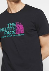 Svart bomullströja med en turkos och rosa grafisk logotyp. Kortärmad och med rund halsringning. Slät textur, standard passform.