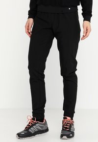 Svarta träningstights med en avsmalnande design, elastisk midja, slät textur och sidofickor, kombinerat med svarta och grå löparskor.