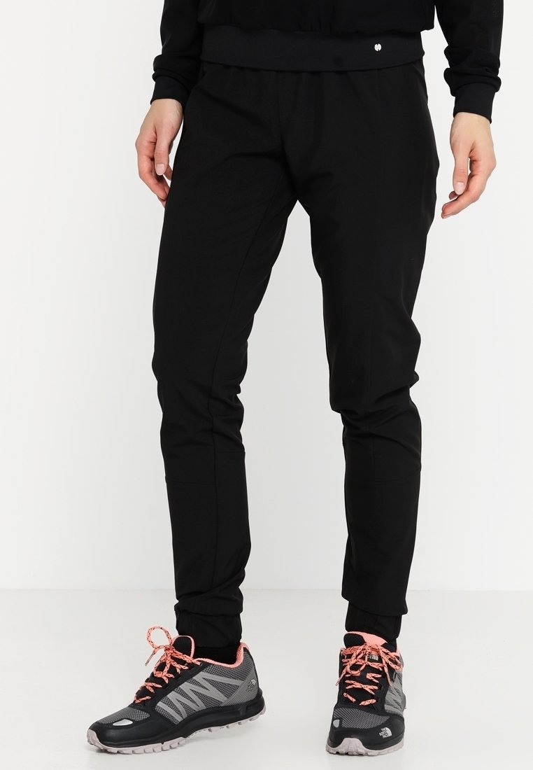 Svarta träningstights med en avsmalnande design, elastisk midja, slät textur och sidofickor, kombinerat med svarta och grå löparskor.