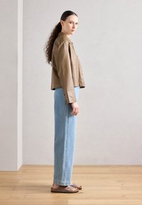Giubbotto cropped in pelle marrone, jeans dritti azzurri chiari e sandali marroni. Texture lisce con hardware minimale e design sartoriale.