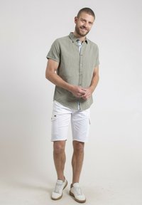 Chemise en lin olive à manches courtes avec fermeture à boutons, assortie à un short cargo blanc et à des baskets blanches avec des semelles marron clair.