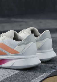 Paire de chaussures de course blanches et grises avec des bandes orange étiquetées « Duramo SL 2 » sur une surface extérieure texturée.