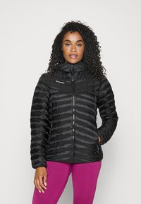 Veste isolée noire avec un col montant, fermeture éclair à l'avant et détails cousus. Le modèle la porte sur des leggings texturés roses.