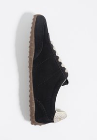 Zapato de ante negro con una suela texturizada marrón, que presenta un sutil acento claro en el talón y costuras decorativas a lo largo de los lados.