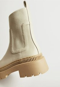 Bottine beige en cuir et tissu avec languette, semelle épaisse crantée et panneaux latéraux élastiques.