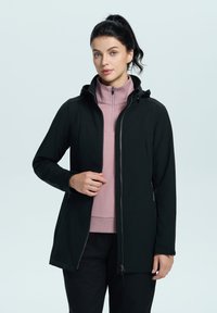 Musta vetoketjullinen takki hupulla vaaleanpunaisten korkeakauluksisten yläosien päällä. Ominaisuuksiin kuuluu slim-muotoinen design, sileä pinta ja sivutaskut.