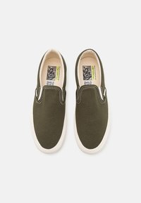 Olivgröna canvas-slip-on-skor med vit gummisula, kontrasterande sömmar och en vadderad krage för komfort.