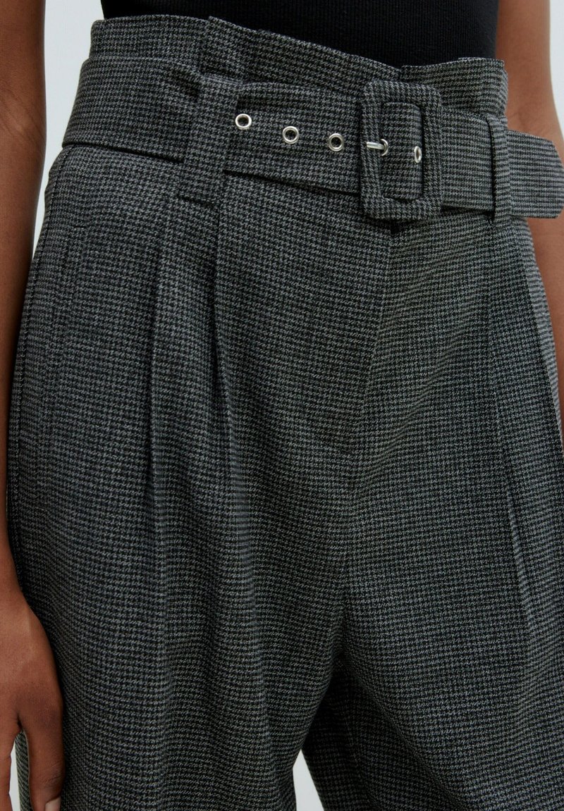 Grau gemusterte, hochgeschnittene Hosen mit einem breiten Gürtel, der eine quadratische Schnalle und mehrere Gürtellöcher aufweist, frontale Falten und strukturierter Stoff.