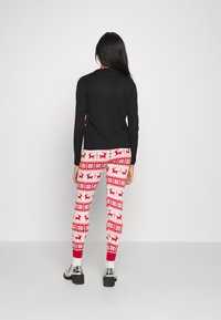 Black long-sleeve top paired with white leggings featuring red reindeer patterns and a red cuff. The leggings have a snug fit and a soft texture.
