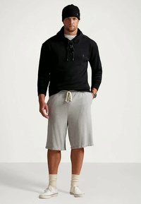 Svart hettegenser med to snorer og logo, grå shorts med elastisk linning, hvite joggesko og svart lue. Casual athletisk antrekk.