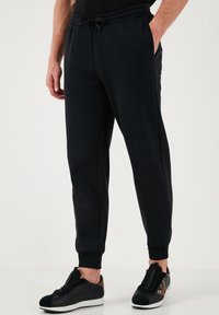 Schwarze Jogginghose aus leichtem Stoff, mit elastischem Bund und Kordelzug, Seitentaschen und engen Bündchen.