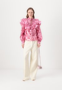 Blusa floreale rosa con dettagli a volant, colletto alto e maniche lunghe abbinata a pantaloni bianchi a gamba larga. Inclusa anche una piccola borsa rosa.