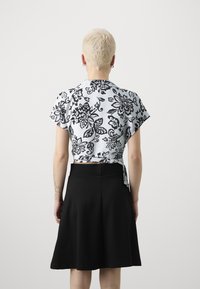 Top a maniche corte con motivo floreale in bianco e nero, con schiena annodata, abbinato a una gonna nera al ginocchio. Tessuto morbido e vestibilità comoda.