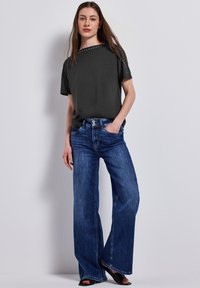 Haut court gris foncé à manches courtes avec des accents cloutés et un jean en denim bleu à jambe large. Texture de tissu lisse, coupe ample et taille haute.