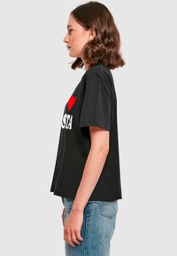 Juodas medvilnės marškinėliai trumpomis rankovėmis, su dideliu baltu tekstu "I ❤️ ISTA" ir raudonu širdies akcentu priekyje.