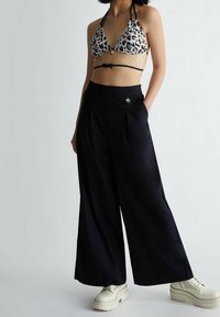 Bikini top w wzór panterki z trójkątnymi miseczkami i czarnymi ramiączkami, w połączeniu z czarnymi, wysokim stanem spodniami o szerokich nogawkach z plisami i akcentem w kształcie gwiazdy.