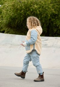 Beige Fleece-Hoodie mit hellblauen gesteppten Ärmeln, kombiniert mit passenden gesteppten Hosen und braunen Ankle-Boots.